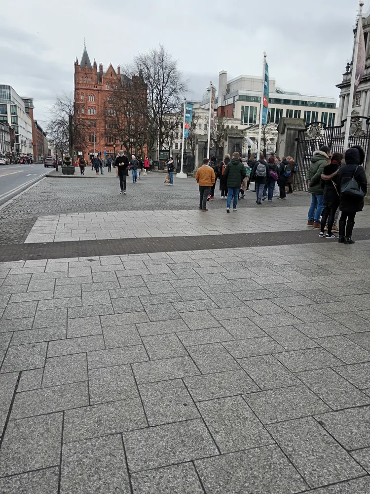 A pedestrianised Belfast city-centre street with red-brick and white buildings and people walking across the paving.